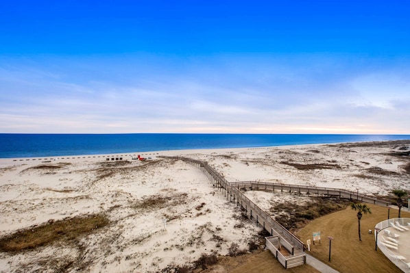 Ein Strand mit einer Holzpromenade, die zu einem Sandbereich führt, einem klaren Himmel und dem Meer im Hintergrund.