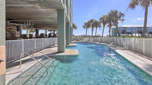 A swimming pool with a concrete deck, metal railings, and palm trees in the background. - Bay View Condo w/ Deck, Assigned Boat Slip, WiFi, AC & Shared Pools/Hot Tubs (Fort Morgan)