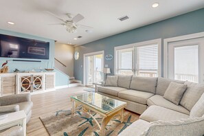 A living room with a sectional sofa, a glass coffee table, a ceiling fan, and a flat-screen TV mounted on the wall. - Beach & Gulf-Front House with Beach Views, Balcony, Central AC (Fort Morgan)