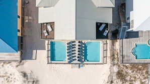 Vue aérienne d’un complexe hôtelier doté d’une piscine centrale, de nombreuses chaises longues et d’une terrasse en bois.