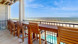 Une terrasse en bois avec une table et des chaises, donnant sur une plage et l’océan.