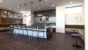 Een moderne bar met een lange toonbank, meerdere barkrukken, hanglampen en een betegelde vloer.