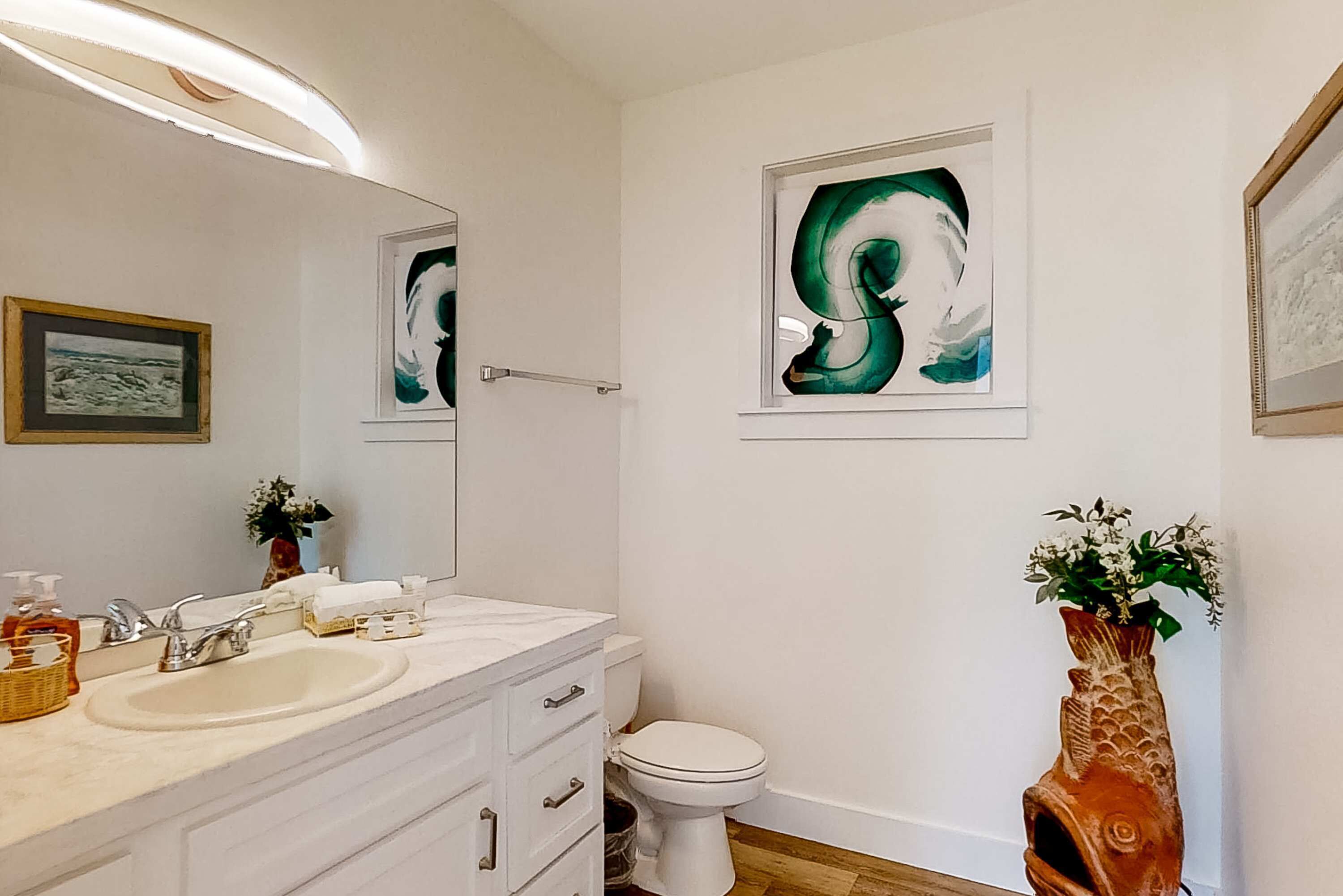 Une salle de bain équipée d’un lavabo, d’un miroir, de toilettes et de deux œuvres d’art encadrées accrochées au mur.