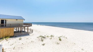 Ett hus vid stranden med en träveranda och ett tak av metall, med utsikt över havet.