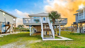 A two-story house with a balcony, a staircase, and a palm tree. - Coastal Living Cottage on Mobile Bay with Private Beach Access (Fort Morgan)