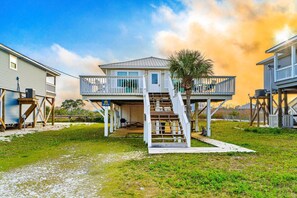 A two-story house with a balcony, a staircase, and a palm tree. - Coastal Living Cottage on Mobile Bay with Private Beach Access (Fort Morgan)