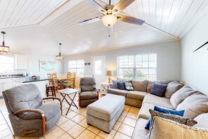 A spacious living room with a ceiling fan, a dining area with chairs, a sofa, and an ottoman. - Coastal Living Cottage on Mobile Bay with Private Beach Access (Fort Morgan)