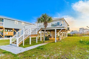 A beachfront property with a wooden deck, a covered outdoor area, and a view of the ocean. - Coastal Living Cottage on Mobile Bay with Private Beach Access (Fort Morgan)