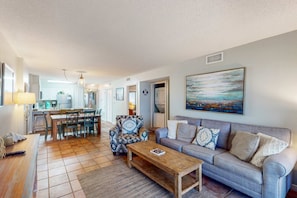 A living room with a sofa, coffee table, and patterned armchair. There is a dining area with a table and chairs. A painting hangs on the wall. - Spacious Oceanfront Home w Open Deck, Free WiFi & Amazing Views (Fort Morgan)