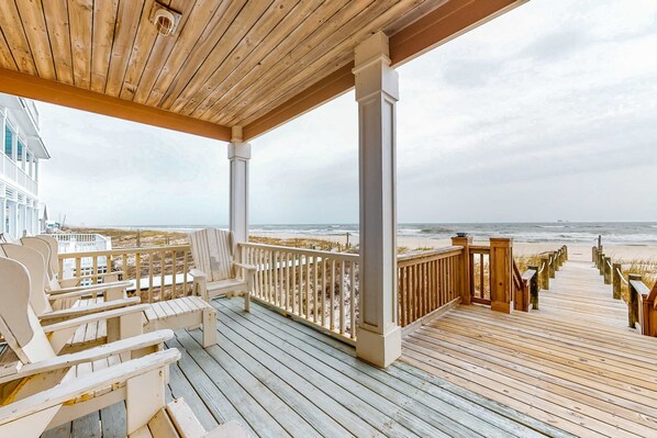 Eine Holzterrasse mit Stühlen und Geländer mit Blick auf den Strand.