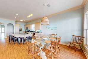 A spacious kitchen with wooden cabinets, a central island, and a dining area with a glass table and wooden chairs. - Spacious 6 BR Gulf Front Home (Fort Morgan)