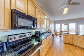 A kitchen with wooden cabinets, a black microwave, a stove, and a coffee maker. - Spacious 6 BR Gulf Front Home (Fort Morgan)