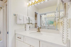 Un baño con tocador blanco, lavamanos, espejo con luces y ducha.