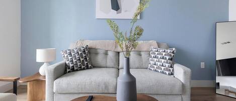 A living room with a sofa, a vase with branches, a remote control, and a lamp.