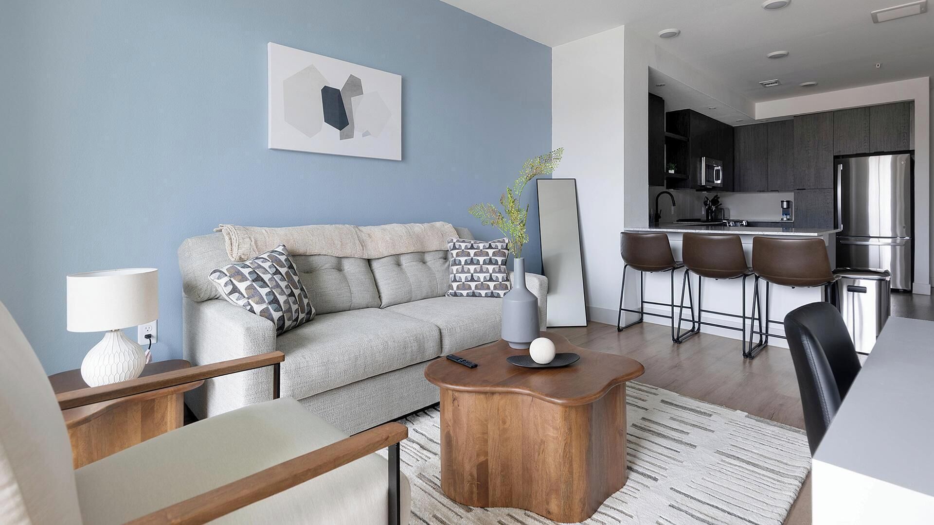 Una sala de estar moderna con sofá, una mesa de centro y una zona de cocina con taburetes de bar.