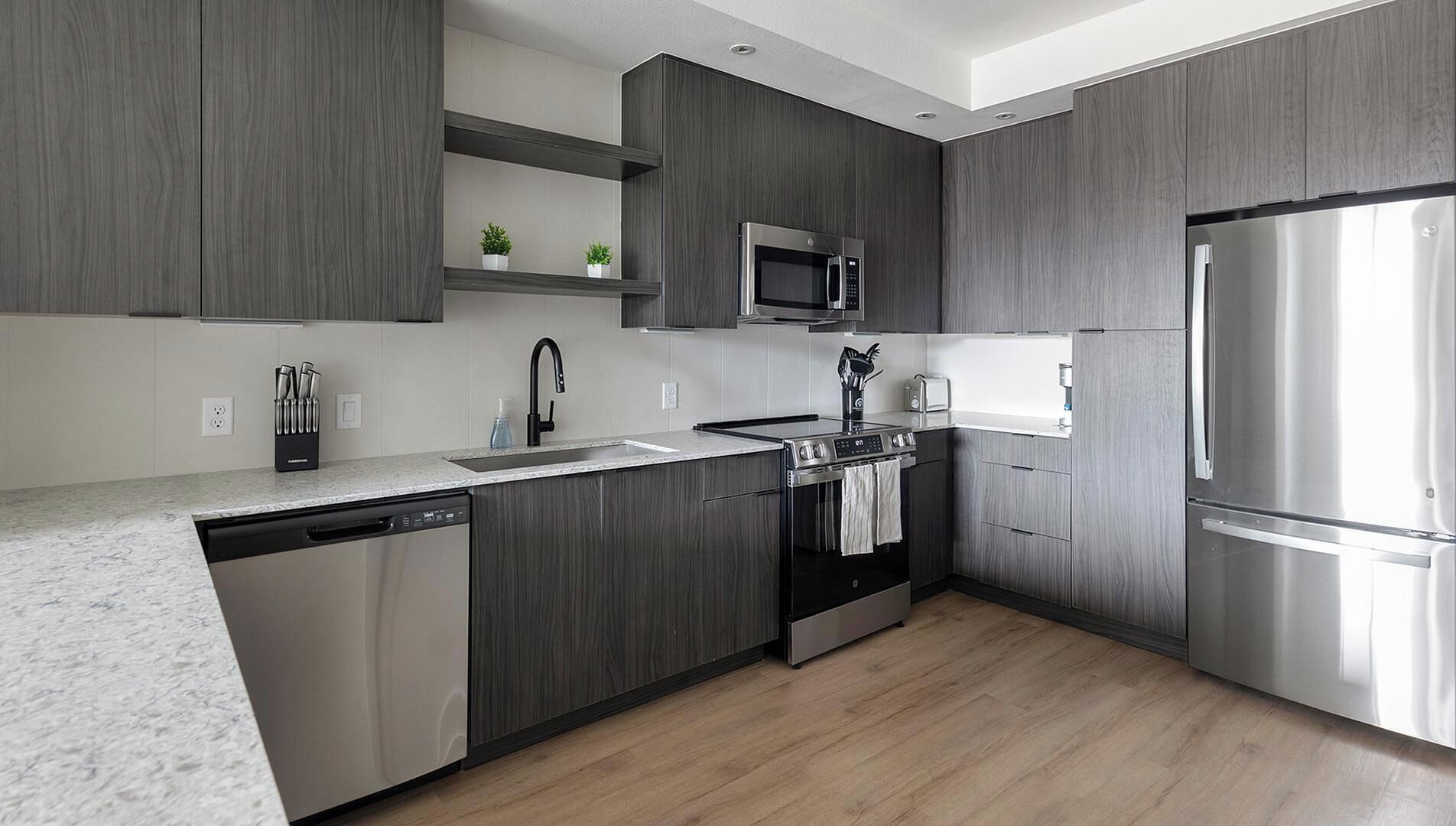A modern kitchen with dark wood cabinetry, stainless steel appliances, and a granite countertop.