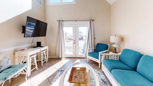 A living room with a TV, a sofa, a chair, a desk, and a window with curtains. - Dog-friendly house with private pool - dock and fishing pier available (Gulf Shores)