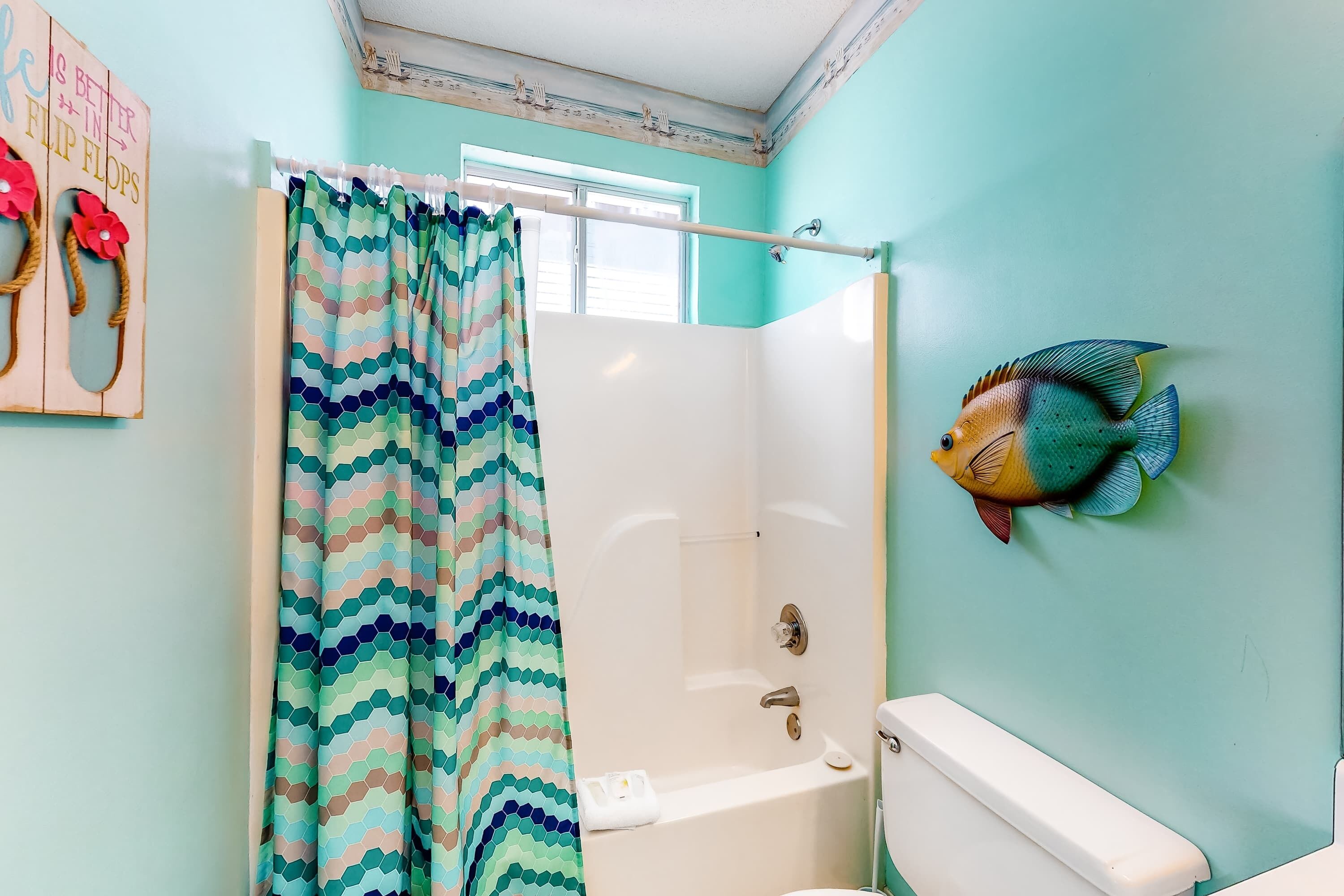 Un baño con cortina de ducha, bañera, inodoro y una decoración de pez en la pared.