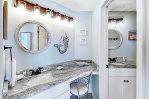 Un baño con lavamanos de mármol, un espejo grande y un perchero para toallas.