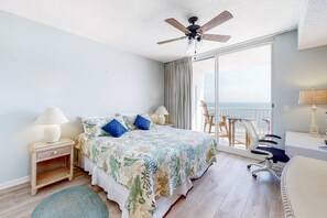 Habitación de hotel con cama, escritorio, silla, ventilador de techo y vista al océano.