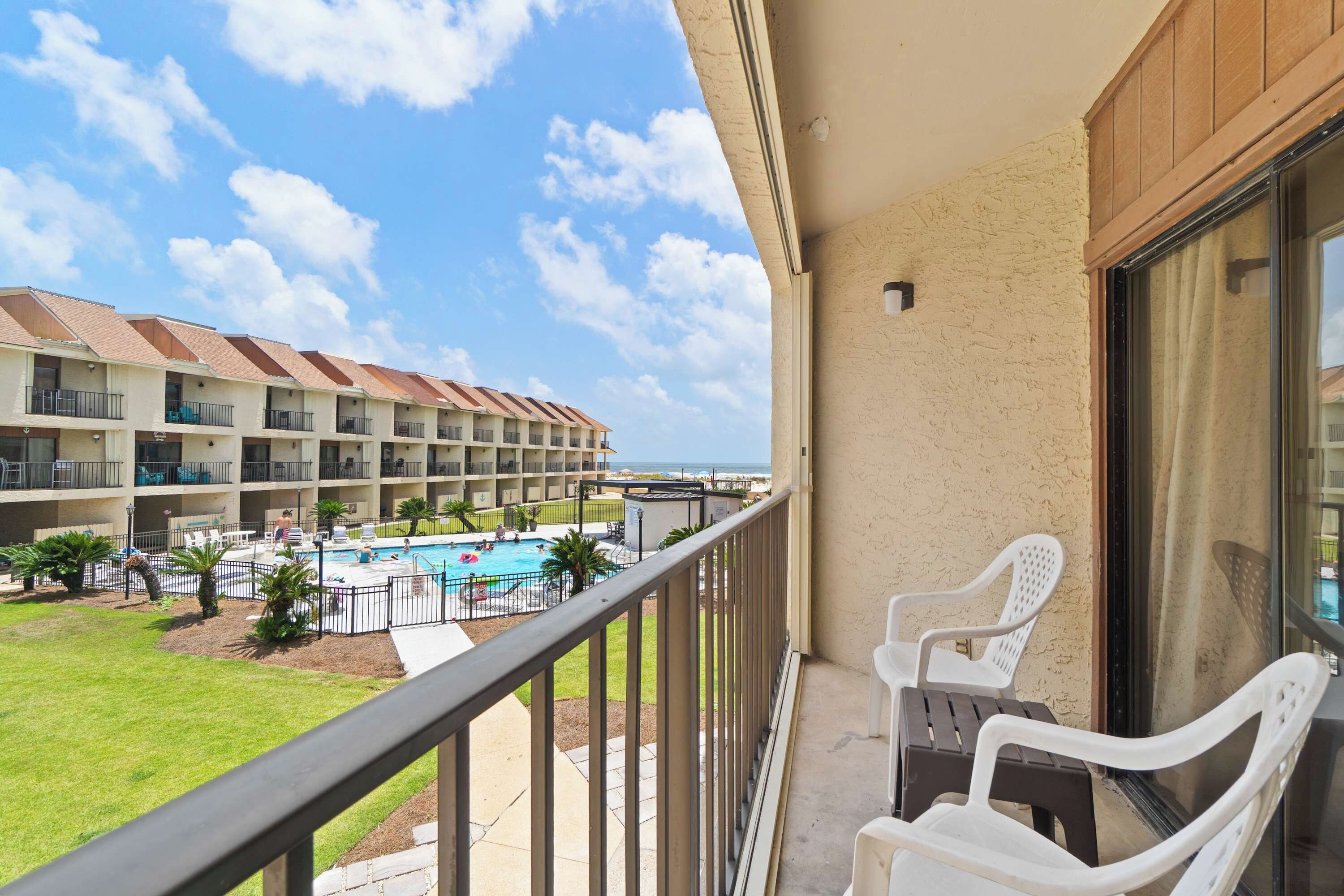 Uma varanda com duas cadeiras de plástico branco, com vista para uma piscina e um edifício de hotel com várias varandas.