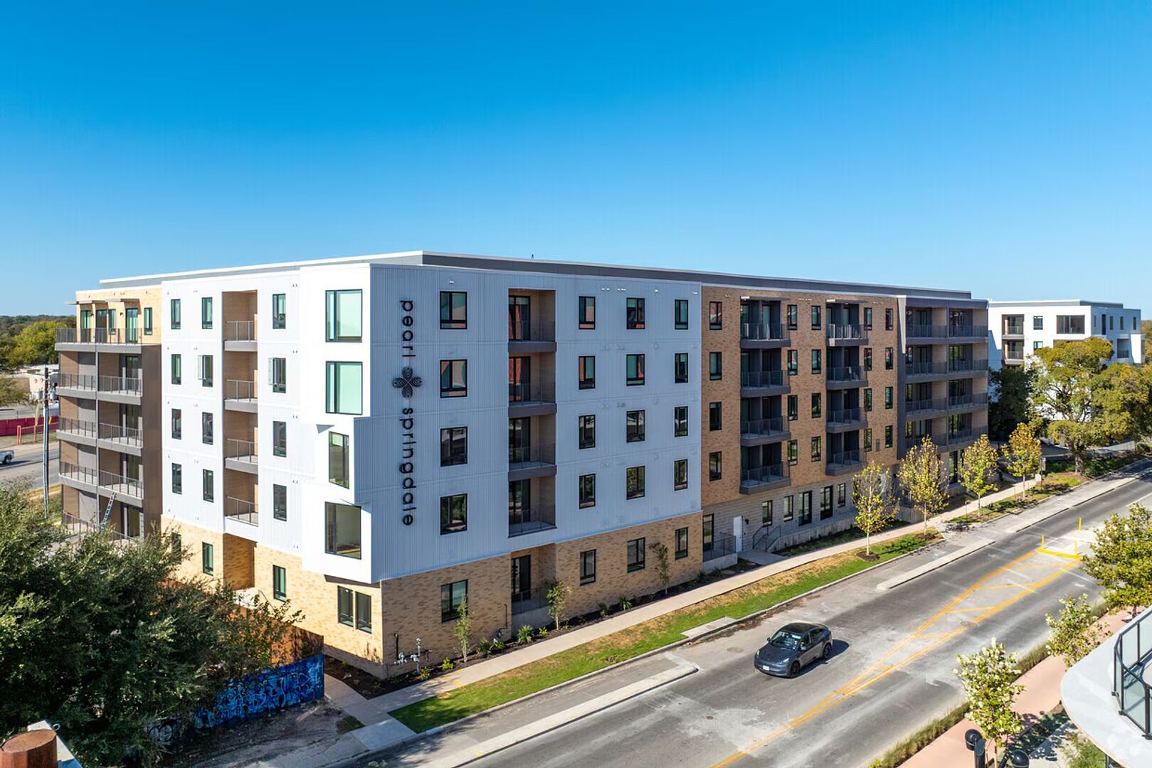 Un immeuble à plusieurs étages doté d’une architecture moderne, caractérisé par un mélange de briques et de murs extérieurs blancs, de nombreux balcons et un ciel dégagé.