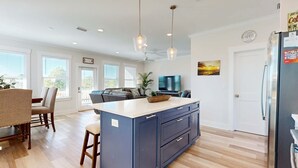 Een moderne keuken met een centraal eiland, houten vloeren, hangende lampen en een koelkast.