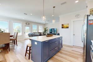 Une cuisine moderne dotée d’un îlot central, de planchers en bois, de luminaires suspendus et d’un réfrigérateur.