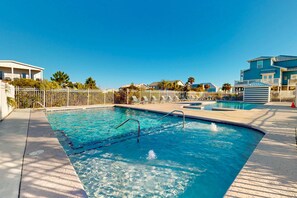 Une piscine entourée d’une clôture blanche, avec une eau d’un bleu limpide et un ciel ensoleillé.