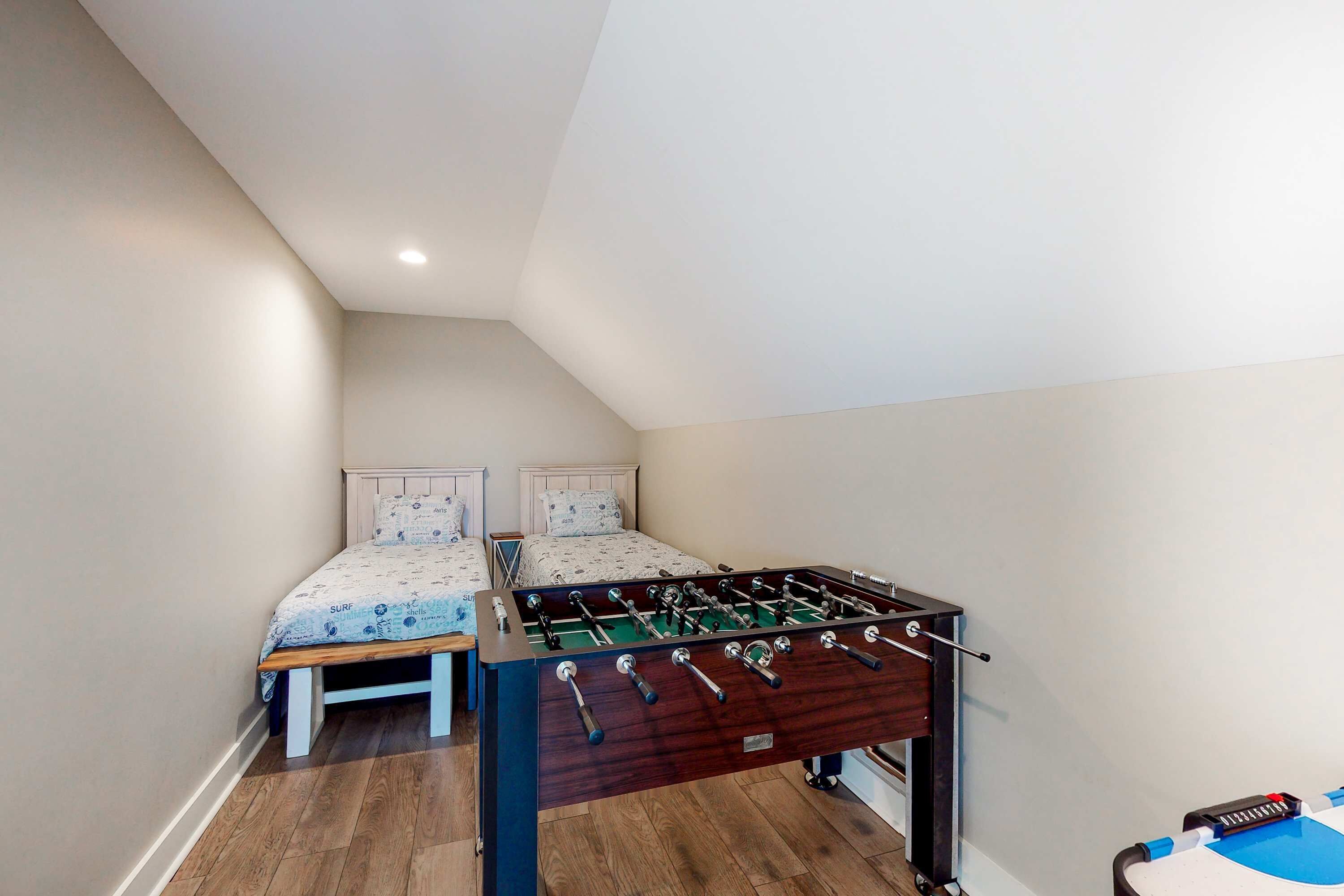 A room with a foosball table, two beds with patterned bedding, and a wooden floor.