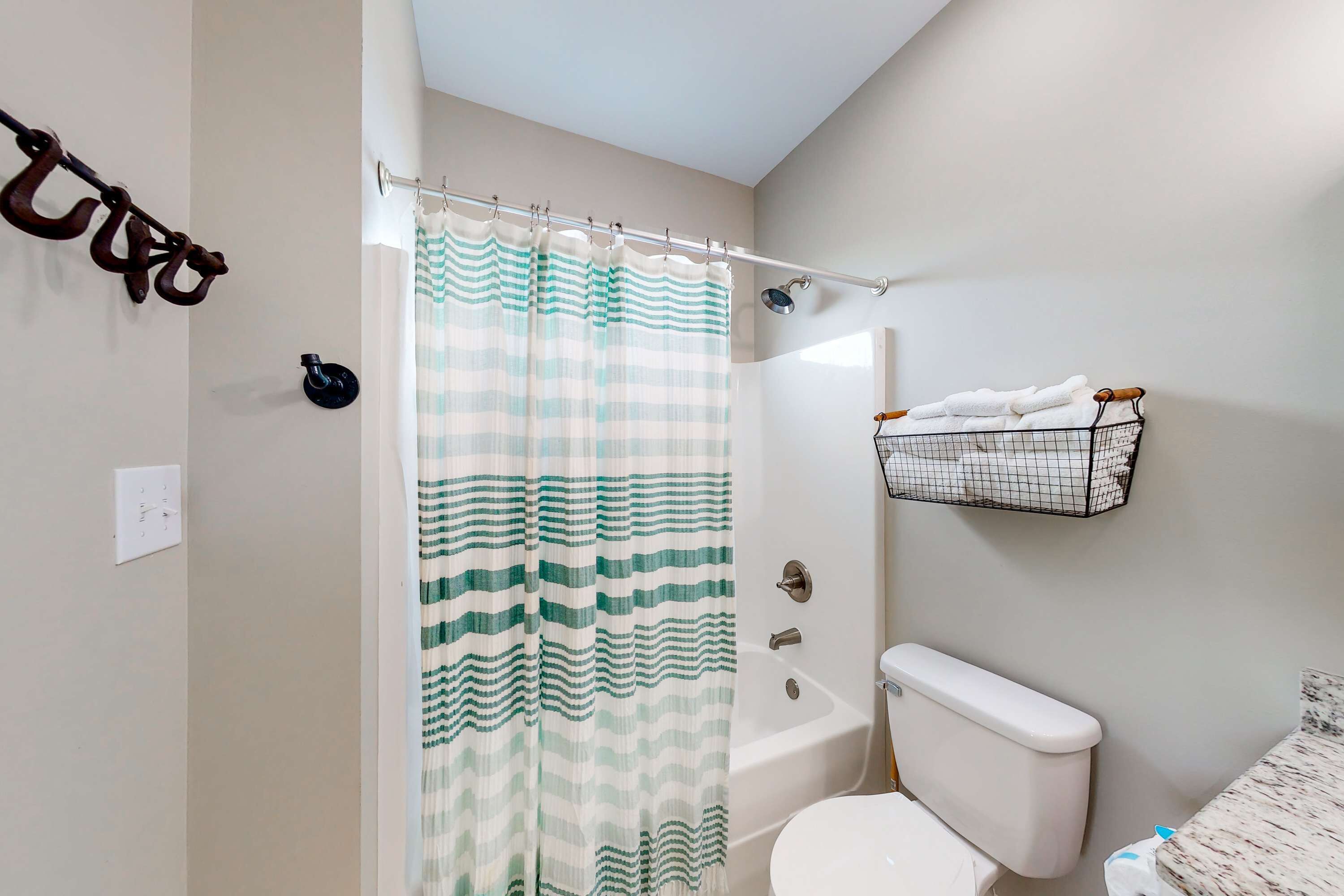 A bathroom with a striped shower curtain, a white toilet, a bathtub, and a towel rack with towels.