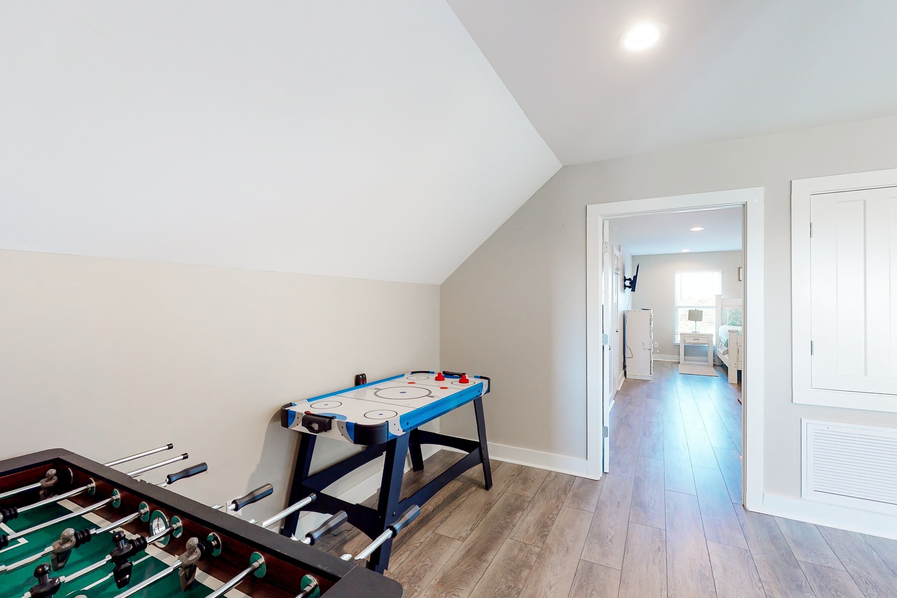 A room with a foosball table, a ping pong table, and a door leading to another room.