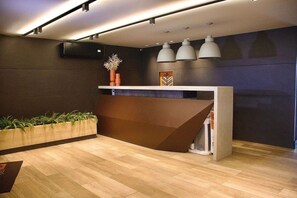 A reception area with a wooden reception desk, a potted plant, and a wall-mounted air conditioner. - Park Del Prado #205 -ape em Cabedelo by Carpediem (Cabedelo)