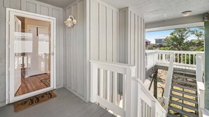 A porch with a white railing, a door leading to a room, and a view of a house in the background. - Newly renovated, bright & chic Home with private deck, grill & near the beach (Fort Morgan)