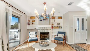 A living room with a fireplace, two chairs, a coffee table, and a chandelier. - Newly renovated, bright & chic Home with private deck, grill & near the beach (Fort Morgan)