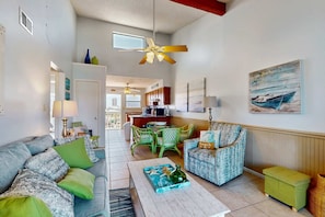 A spacious living area with a sofa, armchair, and coffee table, a dining table with chairs, and a kitchen in the background. - Beautiful condo with shared pools, full kitchen, private washer dryer (Gulf Shores)