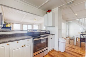 Una cocina con gabinetes blancos, horno de acero inoxidable, encimera de granito y ventilador de techo.
