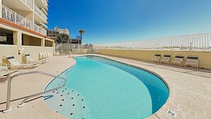 Una piscina con sillones de descanso, una palmera y un edificio con balcones.