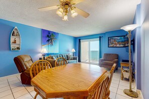 Une pièce avec une table à manger en bois, des fauteuils en cuir, un ventilateur de plafond, un mur bleu, un canapé, une lampe et une fenêtre.