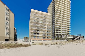 Un hôtel à plusieurs étages doté de balcons, une plage de sable en premier plan et un ciel bleu dégagé.