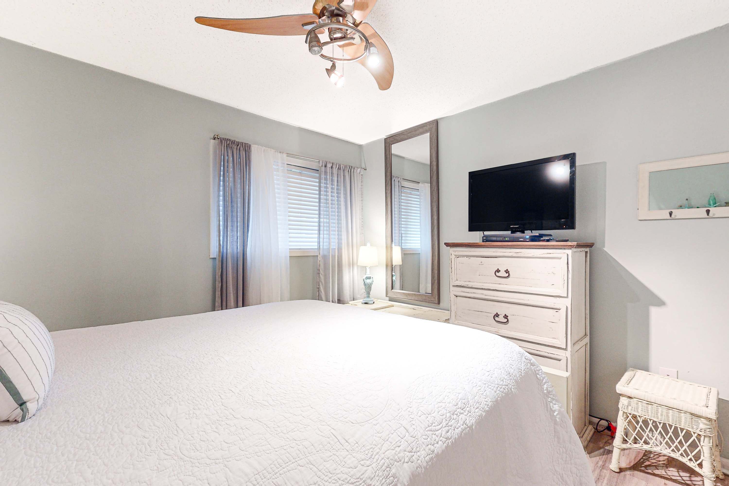 A bedroom with a bed, a ceiling fan, a television, a dresser, and a small stool.