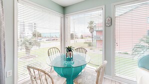 A dining area with a glass table surrounded by chairs, large windows with blinds, and a view of the outside. - Centrally Located Oasis | Pool & Covered Balcony | Walk 1 Block to Beach (Gulf Shores)
