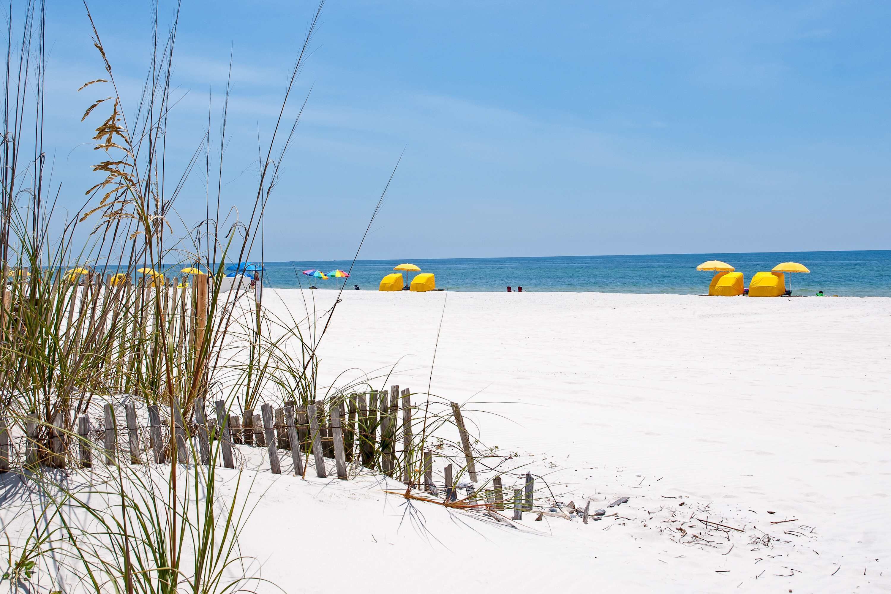 A beach with white sand, yellow umbrellas, and a wooden fence.