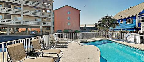 A pool area with lounge chairs, a clear pool, and a building with balconies in the background.