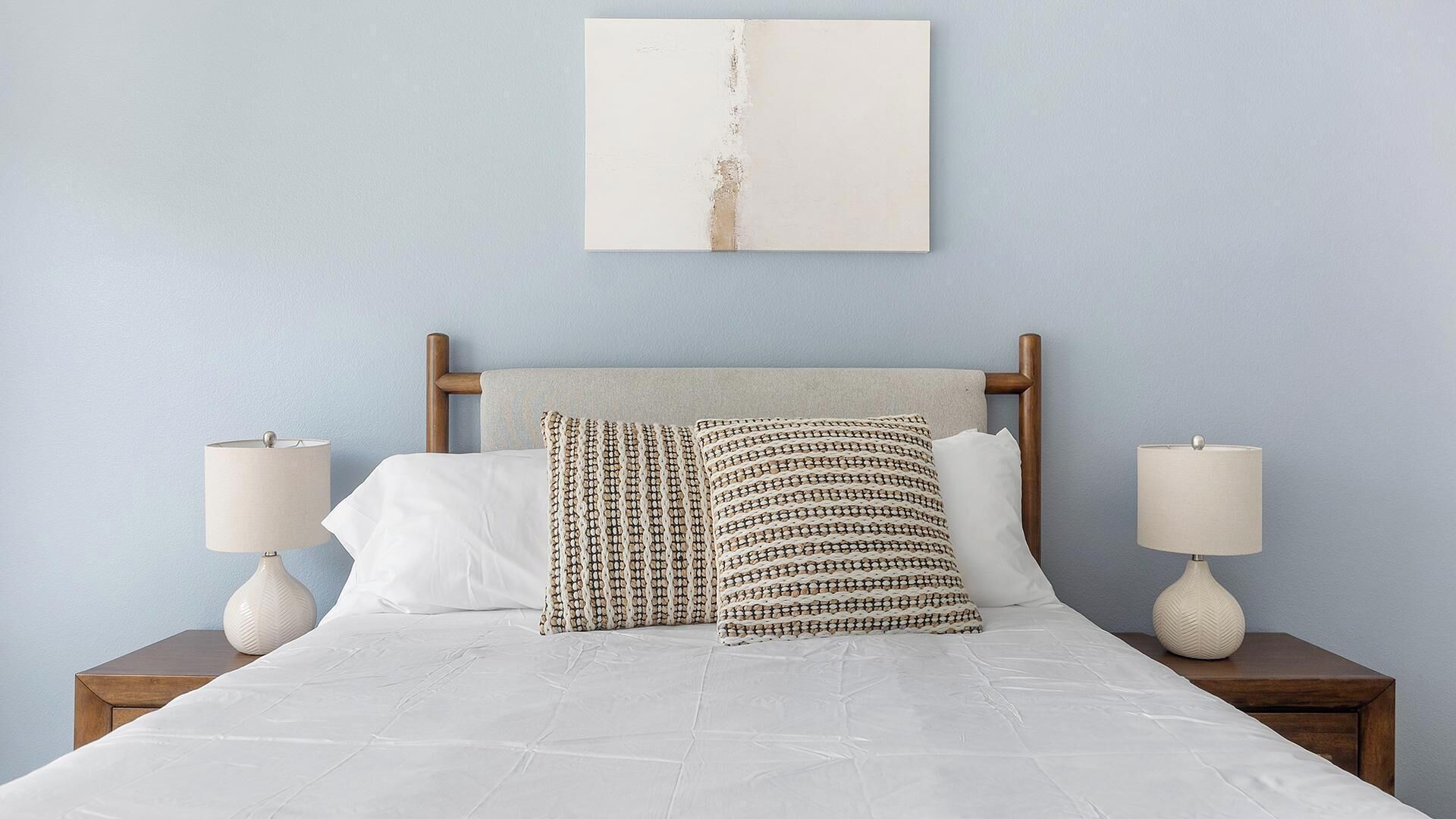 A bed with white bedding, two nightstands with lamps, and a wall-mounted artwork.