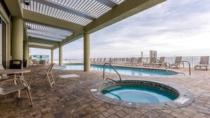 Een dakterras met een zwembad, ligbedden, een jacuzzi en uitzicht op de skyline van de stad.