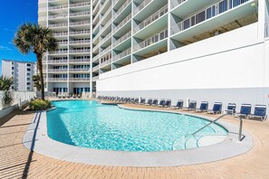 Ein Pool mit Liegestühlen, einer Palme und einem mehrstöckigen Gebäude mit Balkonen.