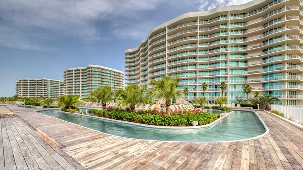 A resort with a pool, wooden deck, and multiple hotel buildings. - Brilliant water view condo with multiple pools, lazy river & internet (Orange Beach)