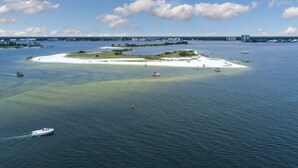 An aerial view of a coastal area with a small island, boats, and distant buildings. - Brilliant water view condo with multiple pools, lazy river & internet (Orange Beach)