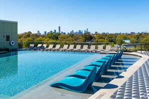 A swimming pool with lounge chairs and a city skyline in the background. - Landing | Chic Studio, Rooftop Lounge, Game Room (Austin)